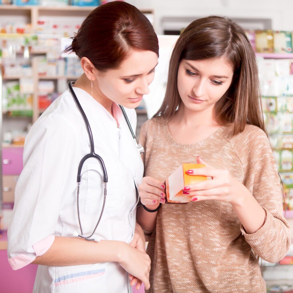 Auxiliar de farmacia orientando a una cliente sobre un medicamento y revisando la información de la caja